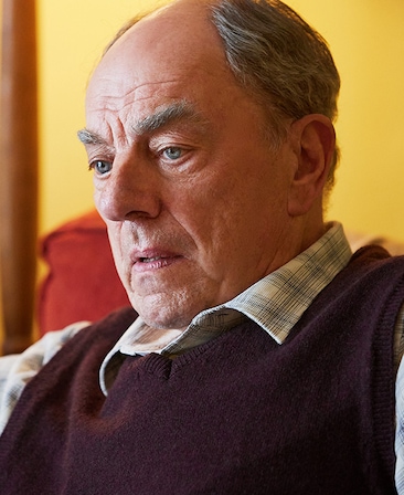 Alun Armstrong headshot wearing a plaid shirt with a burgundy vest.