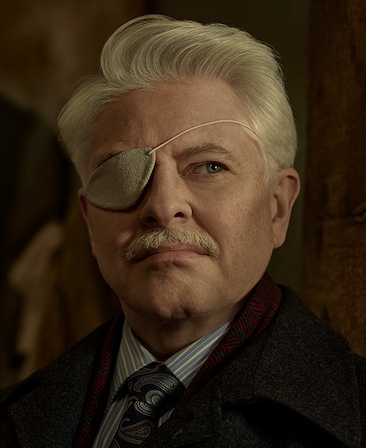 Dave Foley headshot wearing a suit and an eyepatch over his left eye