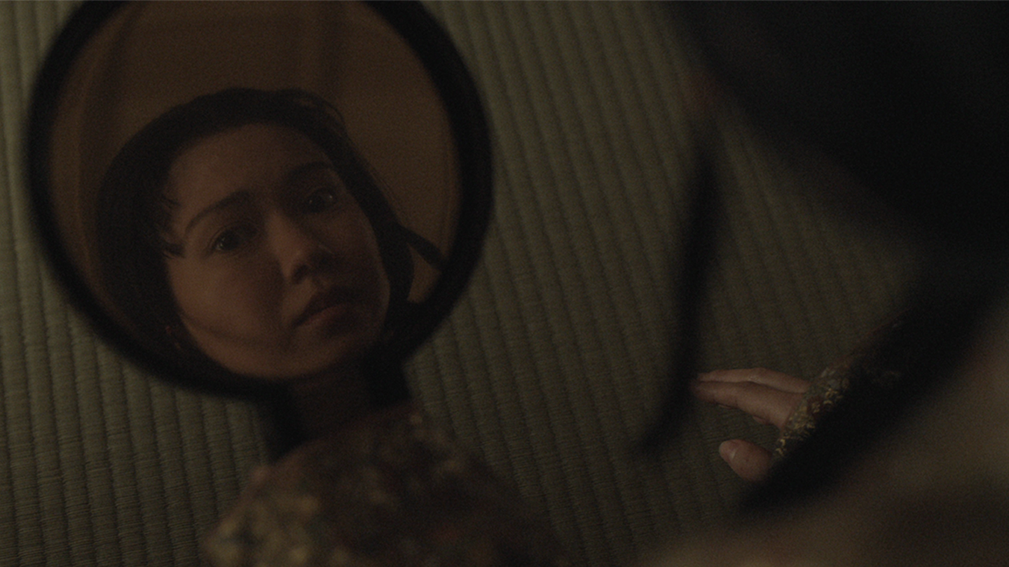 Close up of Lady Ochiba looking into handheld round mirror