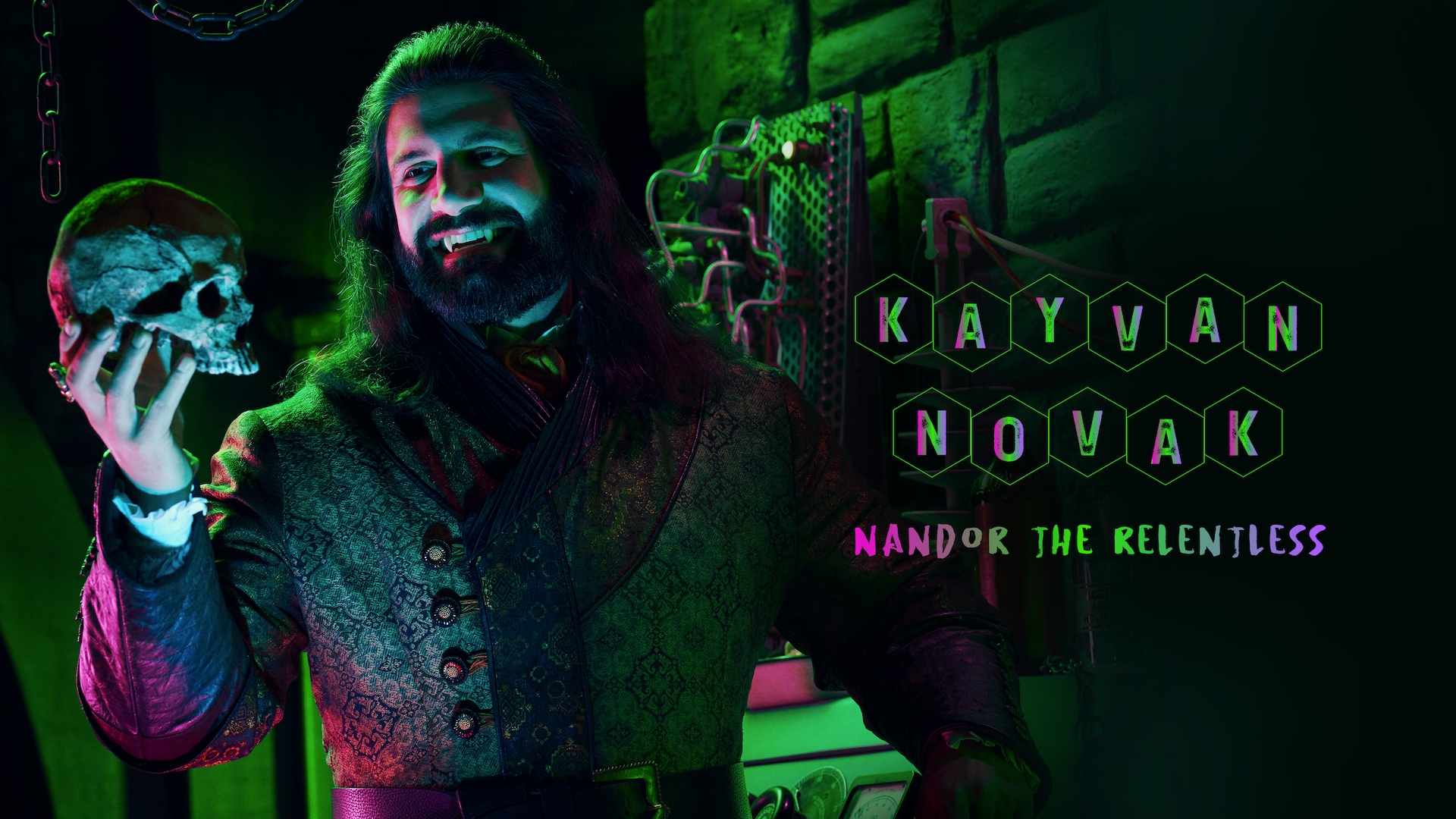 Kayvan Novak as Nandor the Relentless headshot with fangs, wearing a pink striped top holding a skull.