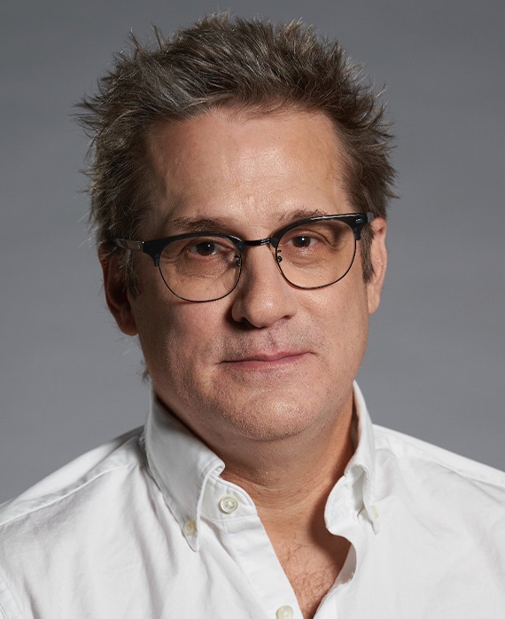 Paul Simms headshot wearing glasses and a white button down shirt.