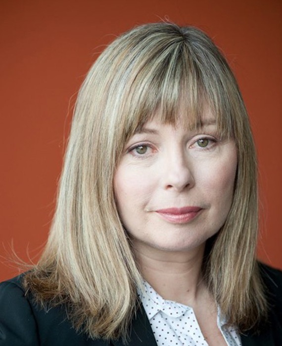 Kim Todd wearing a polka dot shirt with a black jacket, standing against a orange background