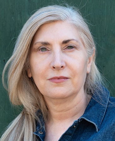 Alice Nutter headshot wearing a denim shirt and standing in front of a green wall