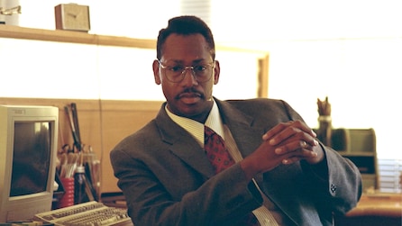 Black man in vintage office with older computer in grey suit with hands crossed and glasses in FX's Atlanta