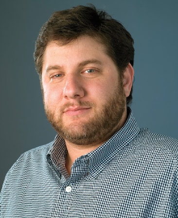 Michael Rosenberg headshot wearing a navy and white plaid shirt with white button