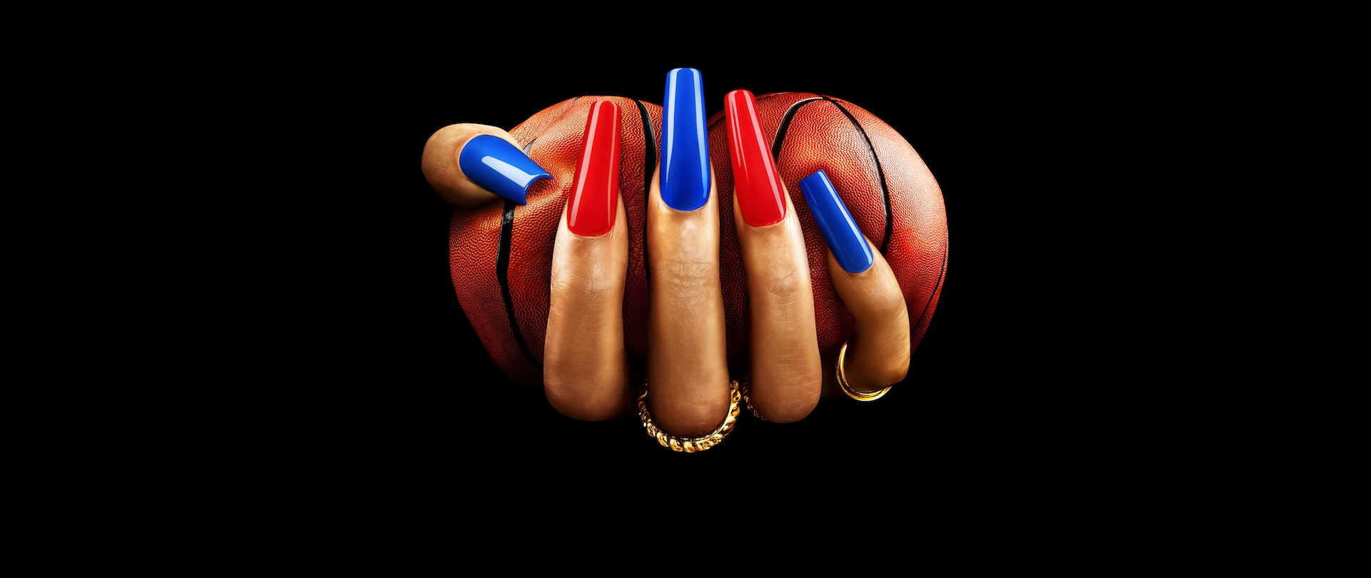 Manicured hand with long blue and red nails squeezing two basketballs