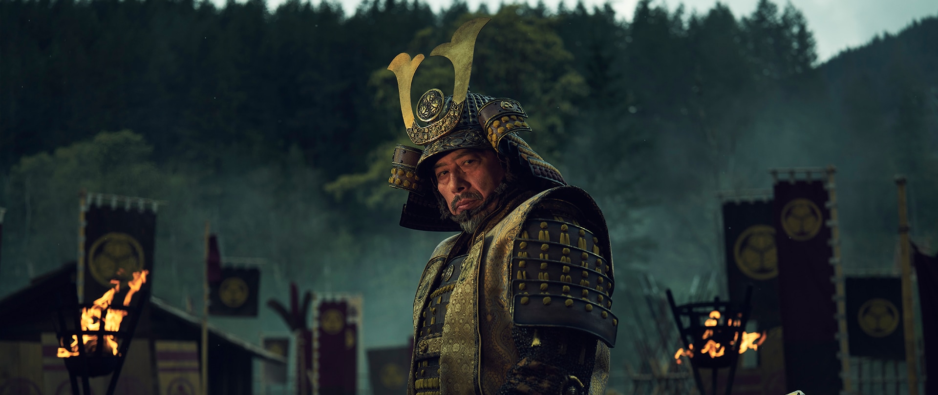 Lord Toranaga in full busho armor standing in front of his war camp amid torchlights