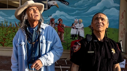 Old Man Fixico and Officer Big looking up into the sky with a mural in the background. 