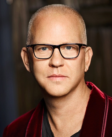 Ryan Murphy headshot in red velvet suit and black glasses.