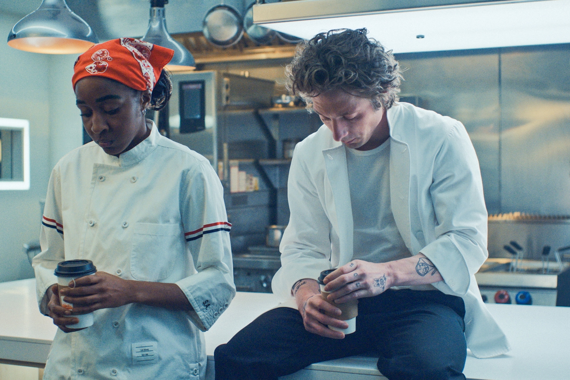 Ayo Edebiri as Sydney and Jeremy Allen White as Carmy holding coffee to go cups in The Bear kitchen with heads lowered