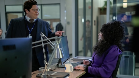 Guillermo pointing at Nadja as she is sitting at her desk in an office setting.