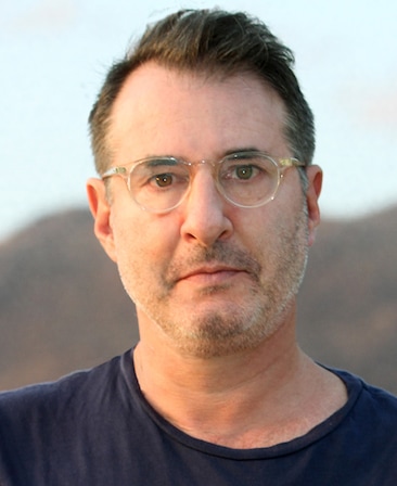 Headshot of Jon Robin Baitz, Executive Producer of FX's Grotesquerie, wearing a navy blue t-shirt and clear rounded glasses.
