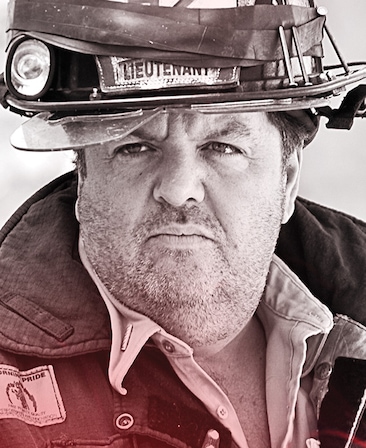 John Scurti headshot wearing a "lieutenant" fireman hat and fire jacket