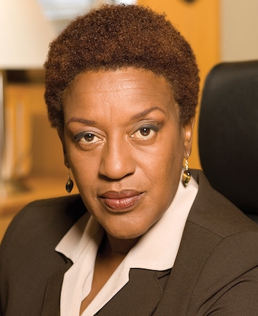 cch pounder headshot wearing a white shirt with a collar and a brown jacket with gold earrings