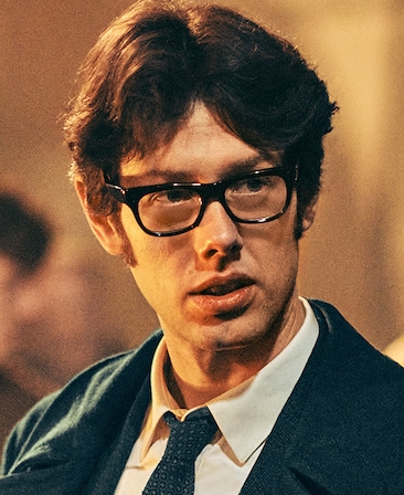 Josh Finan as Gerry Adams in FX's Say Nothing, wearing a dark suit and black glasses.