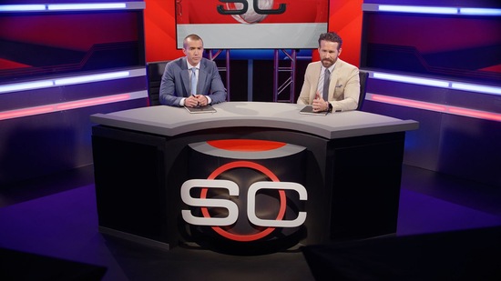 Ryan Reynolds and Rob McElhenney sitting at a talk show desk with the letters SC written across it