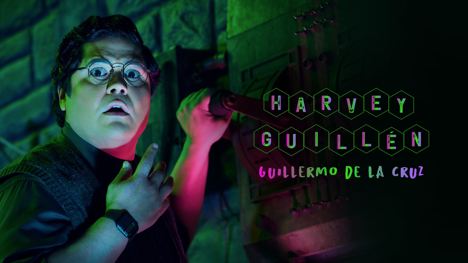 Harvey Guillen as Guillermo de la Cruz in a pink and green lit laboratory with his hand on a large switch.