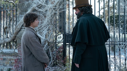 Fionn Whitehead and Matt Berry talking by a big gate with snow covered branches