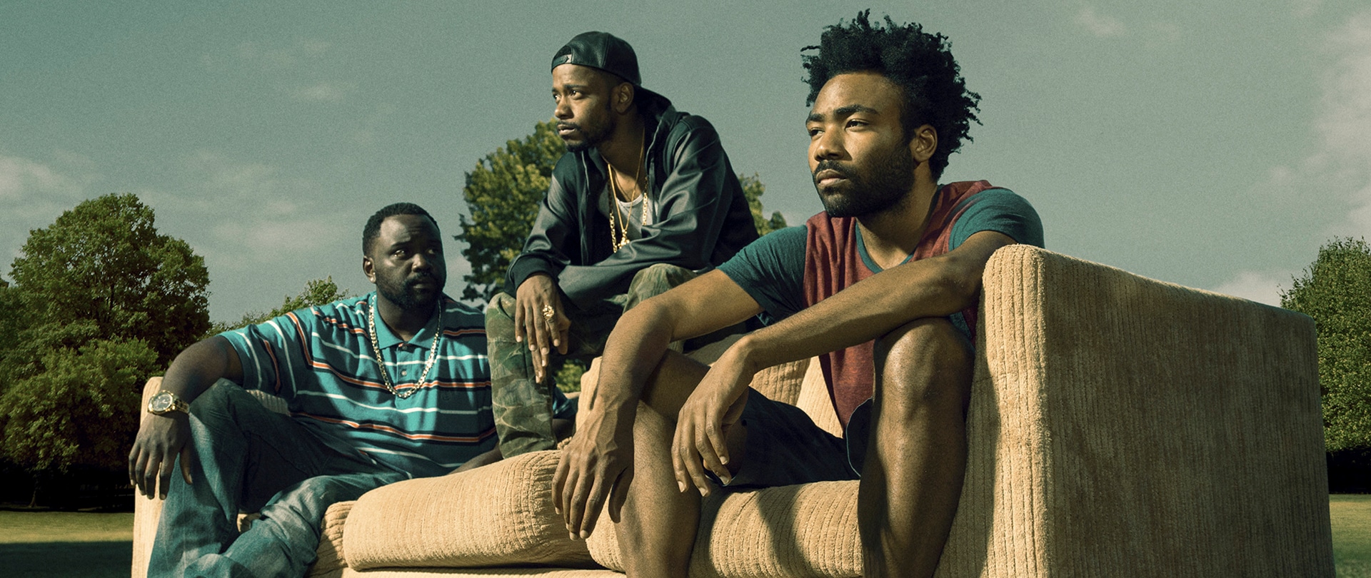 Cast of FX's Atlanta sitting on a tan couch in the middle of a park.