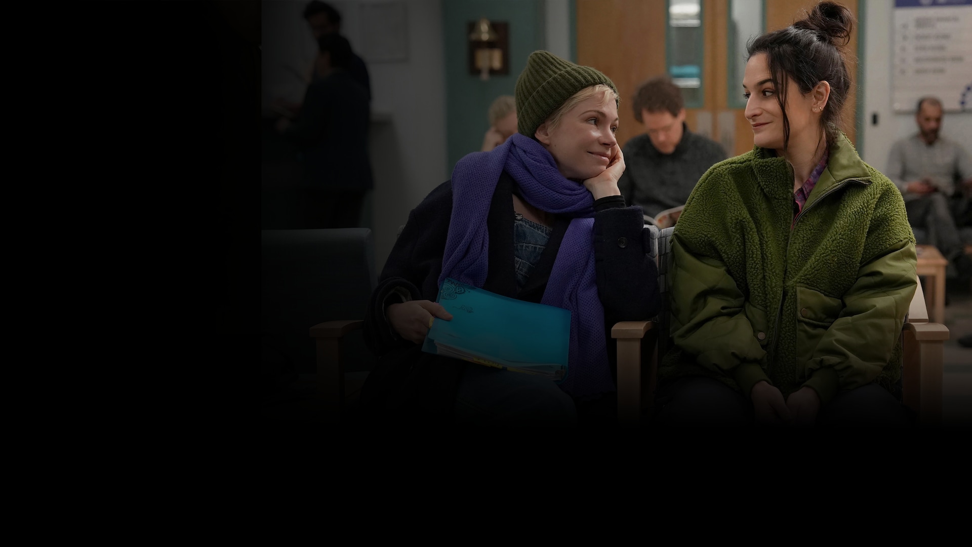 Molly and Nikki sitting in a waiting room looking at each other and smiling. 