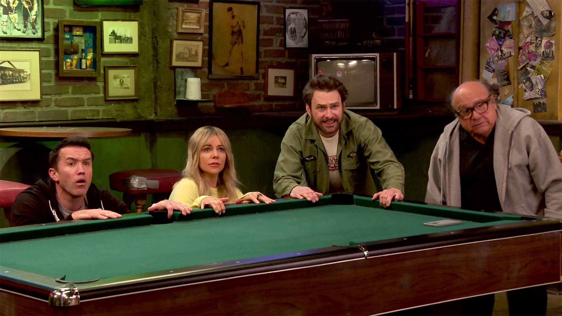 Cast of FX's It's Always Sunny in Philadelphia holding onto a pool table in Paddy's Pub.
