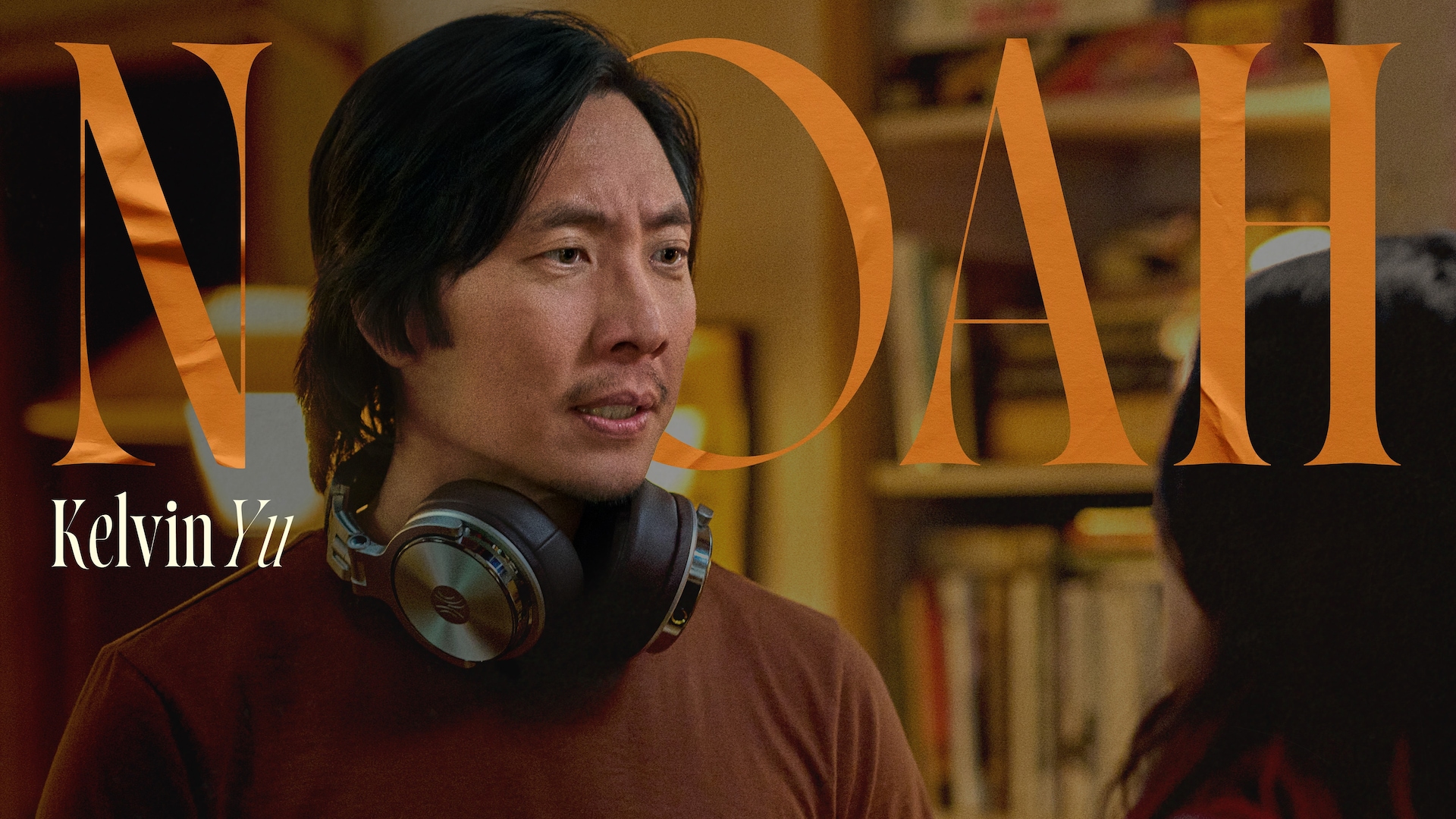 Kelvin Yu as Noah in FX's Dying For Sex, wearing a brown shirt and silver, large headphones around his neck.