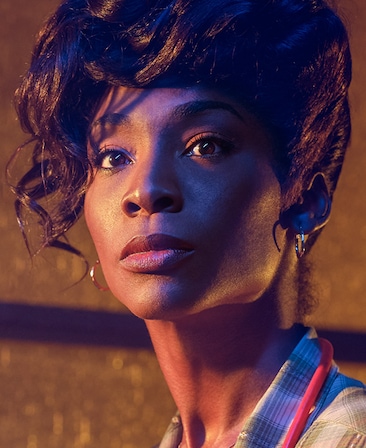 Angelica Ross headshot with hair styled up with gold hoops and plaid blazer from American Horror Story 1984