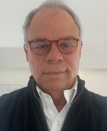 Headshot of Edward McDonnell in a white button up and black coat wearing multicolored glasses.