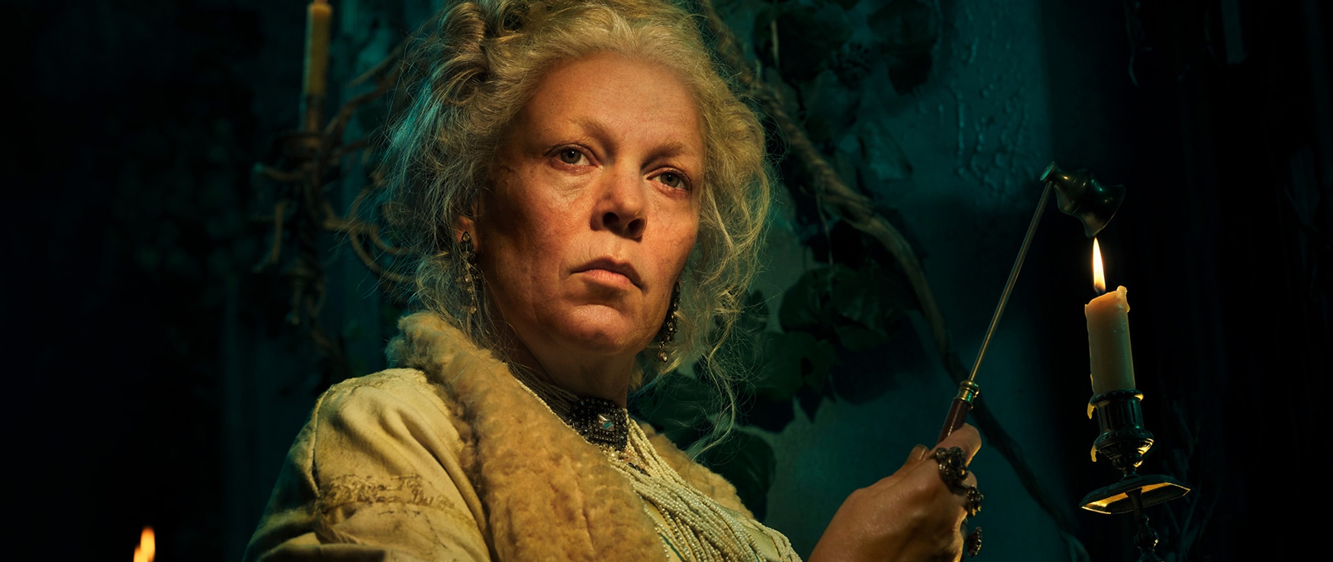 Olivia Colman holding a candle with a serious expression on her face