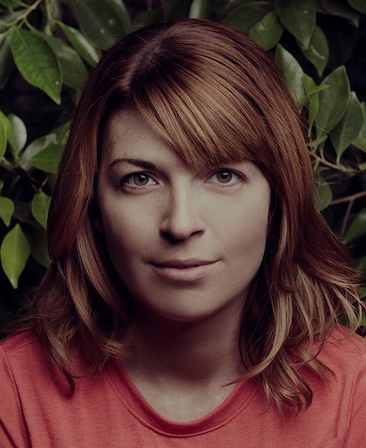 Megan Ganz headshot wearing a red shirt with green leaves behind her