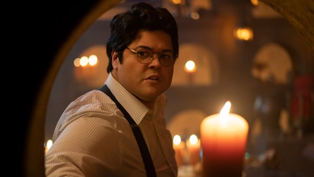 Guillermo wearing a white button down and black suspenders with candles in the background