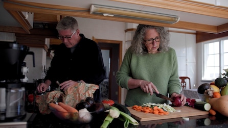 An older man and woman cutting up vegetables in the kitchen