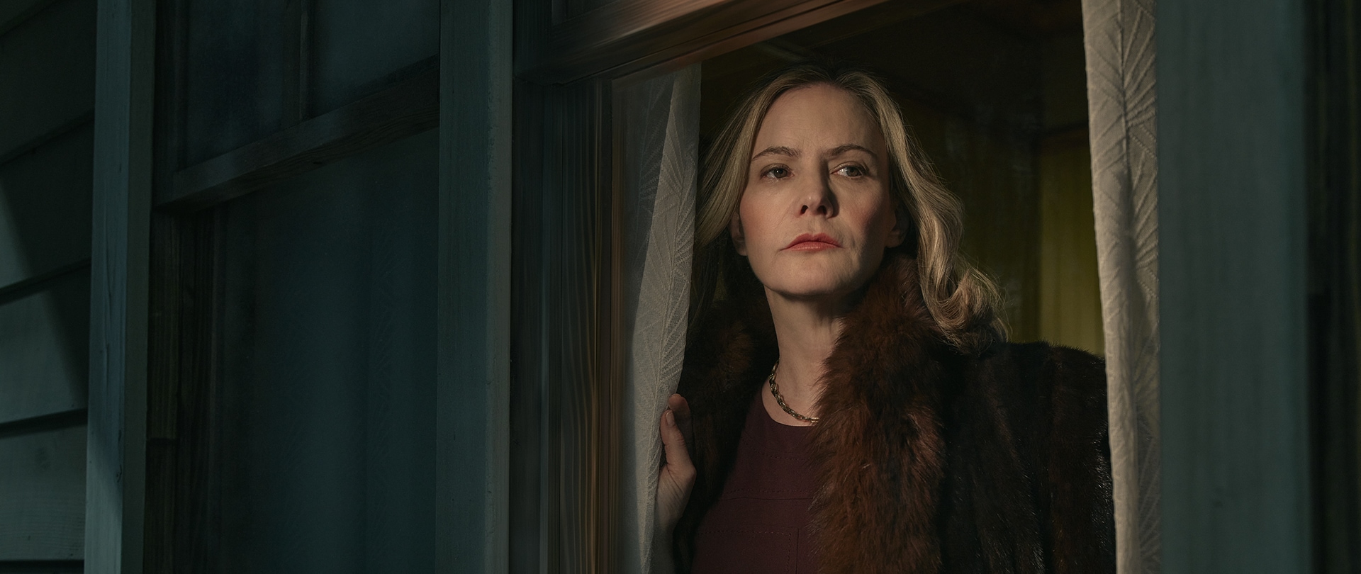 Woman with blonde hair looking through curtain windows