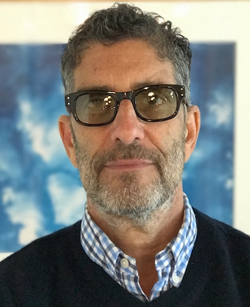 David Schiff headshot wearing black glasses with a blue plaid collar shirt and navy sweater