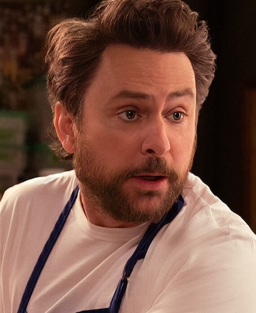 Charlie Day headshot wearing a white shirt and dark blue apron