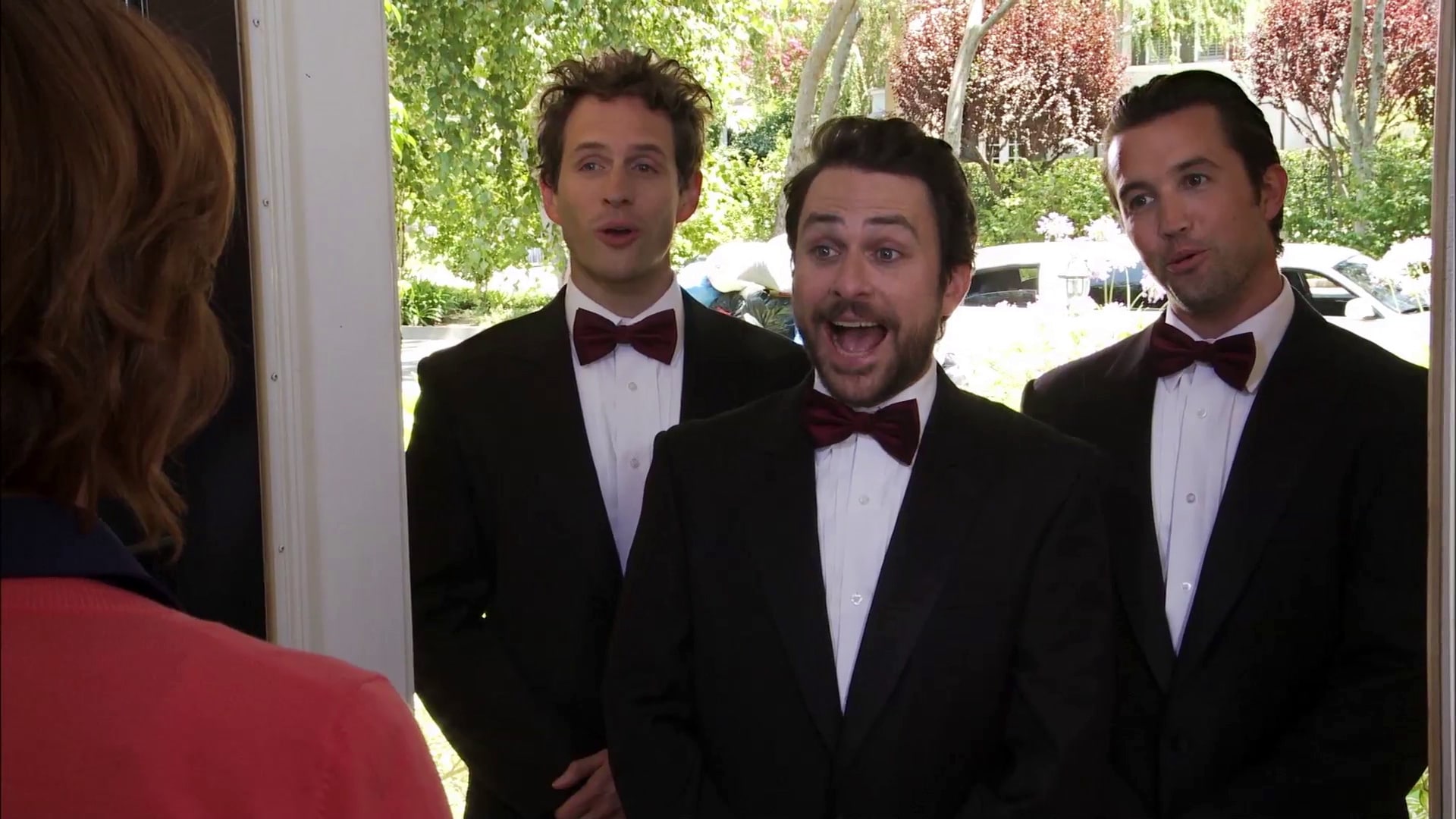 Mac Charlie and Dennis wearing tuxedos with red bow ties and standing in a doorway