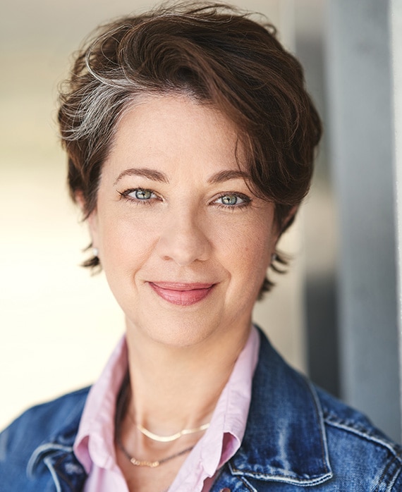 Melanie Marnich headshot wearing a denim jacket and a pink shirt