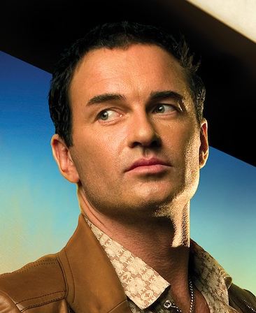 Julian Mcmahon headshot wearing a silver necklace and brown leather jacket