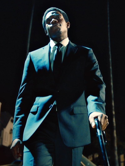 Damson Idris walking in the dark with a suit on and gun in hand