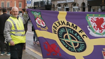Man in a yellow reflective vest holding up a Wrexham flag