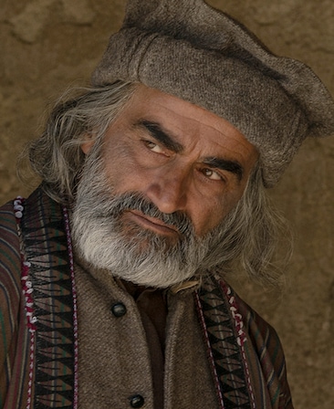 Navid Negahban wearing brown garments against a rocky hill