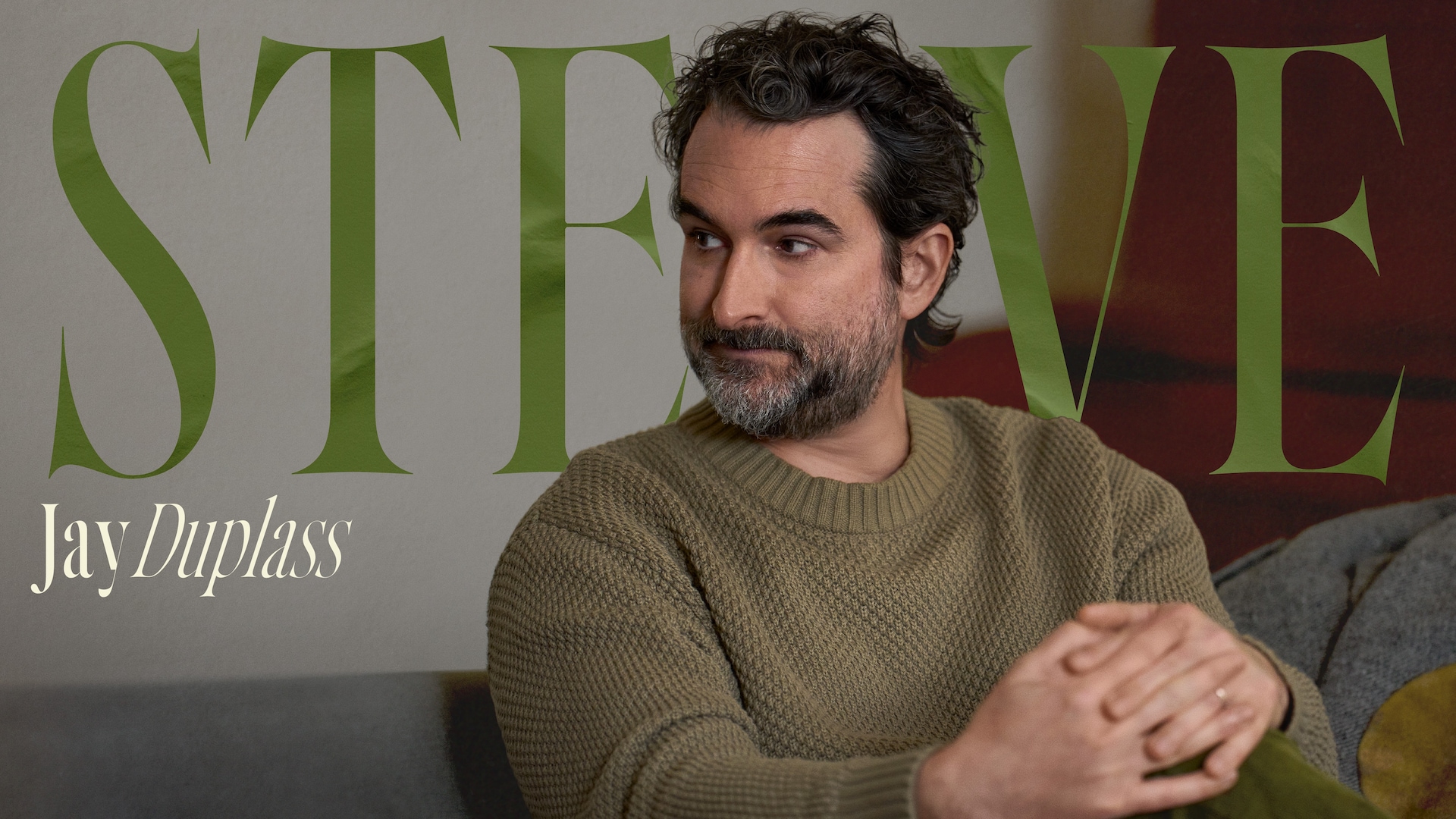 Jay Duplass as Steve in FX's Dying For Sex, sitting down, wearing a green sweater and his hands clasped on his knee.