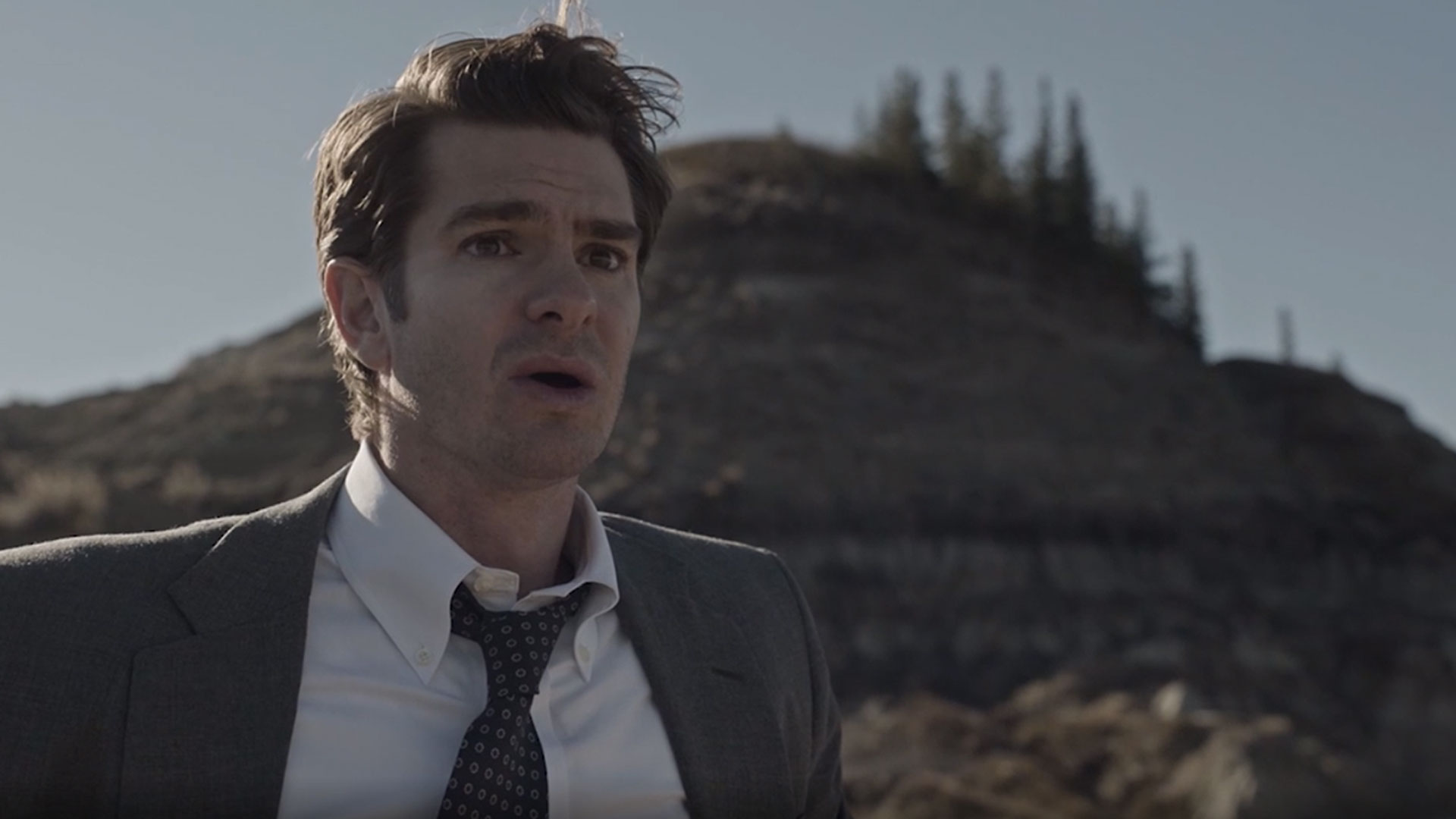 Andrew Garfield standing in the middle of no where wearing a suit and tie