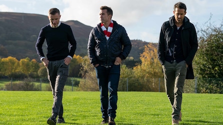 Three men walking together across a green patch of grass