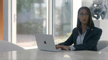 Woman wearing a suit sitting by a window at a table with a laptop 