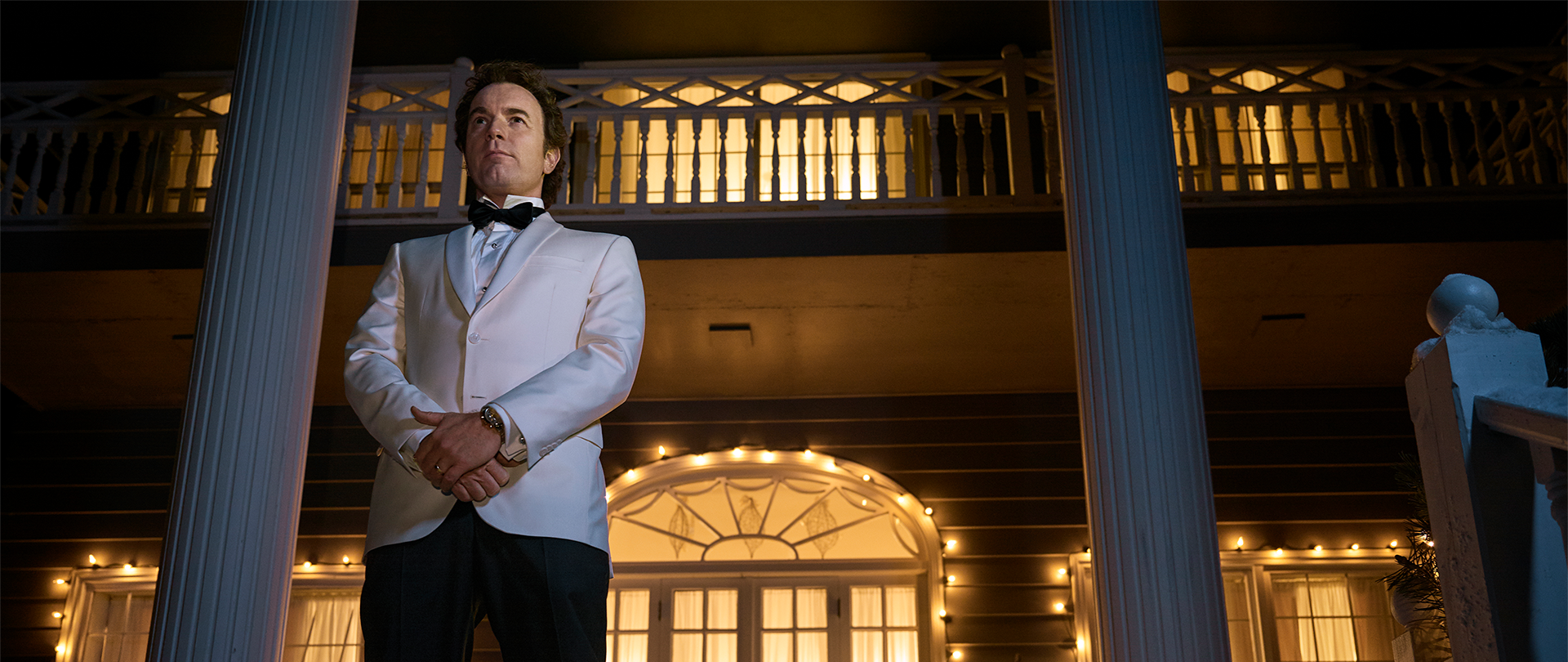 Ewan McGregor as Emmit Stussy standing on the porch of a mansion in a white tuxedo.