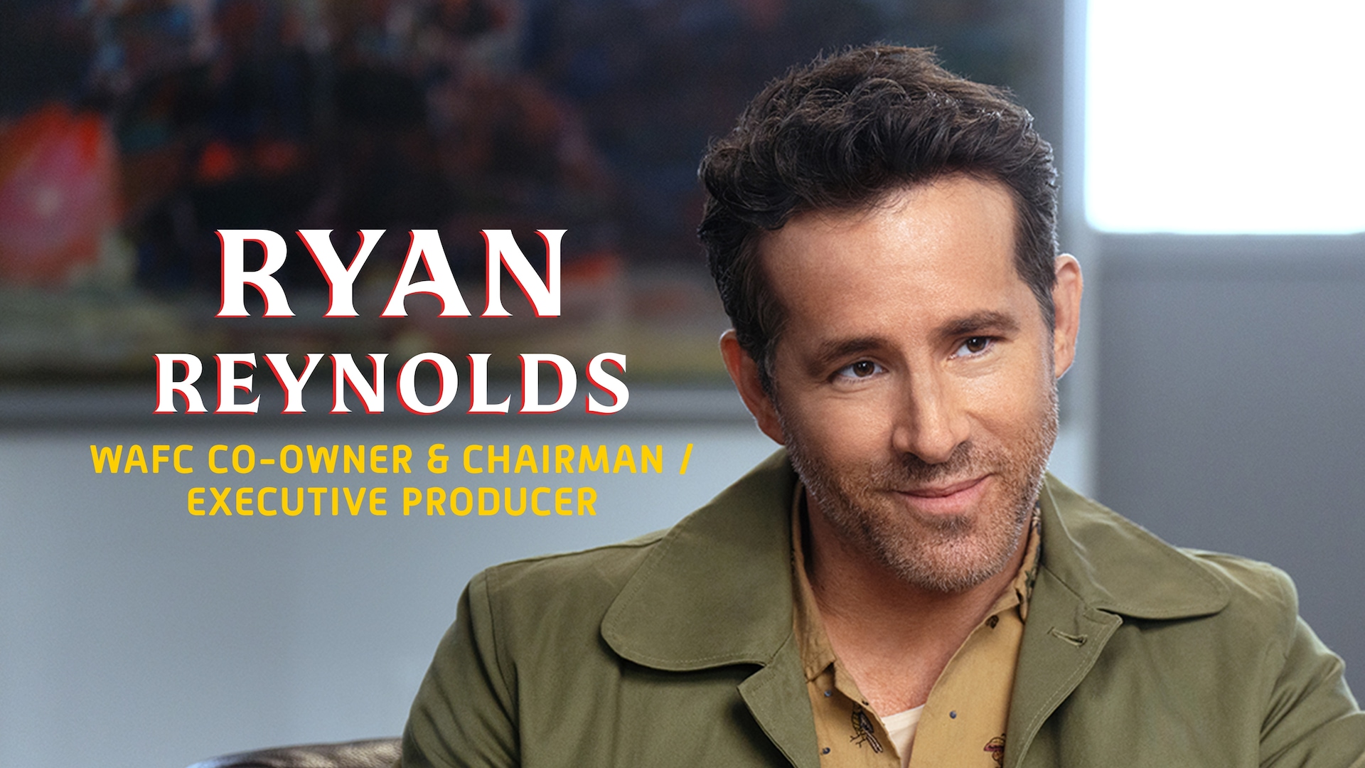 Ryan Reynolds Headshot wearing a green jacket with a Wrexham logo a tan button up underneath with his name in white text.