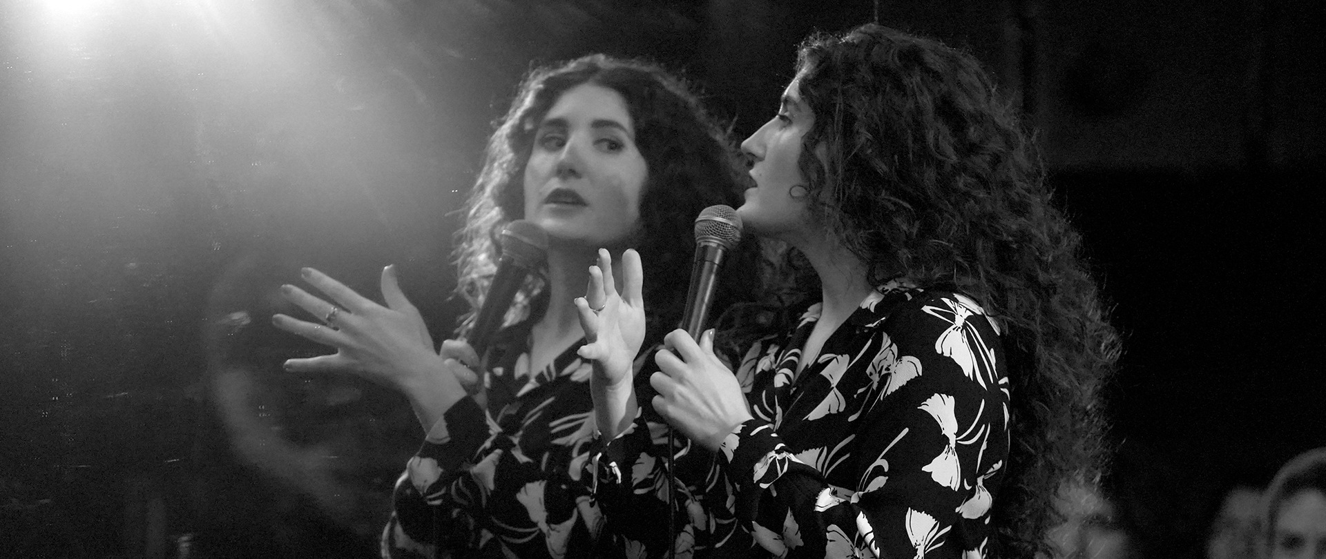 Kate Berlant on stage looking in a mirror with a mic
