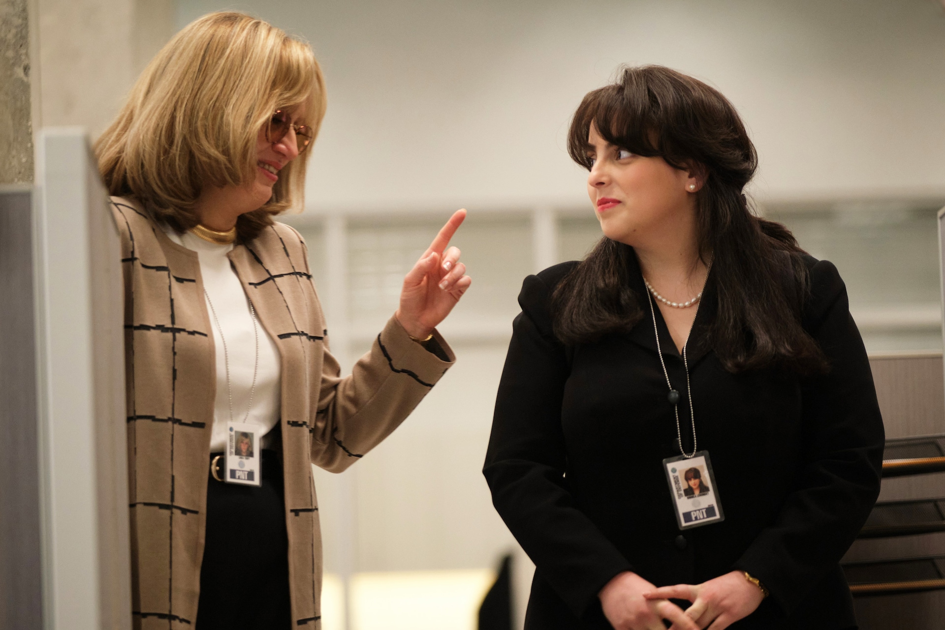 Sarah Paulson as Linda Tripp pointing finger and smiling at Beanie Feldstein as Monica Lewinsky in a hallway