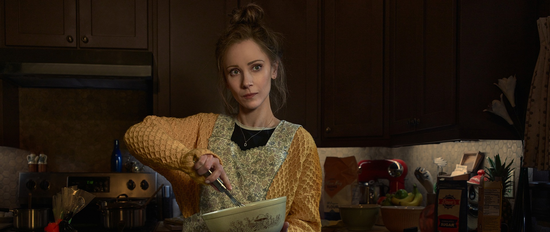 Juno Temple as Dorothy Dot Lyon wearing a patterned apron, using a mixing bowl in a kitchen